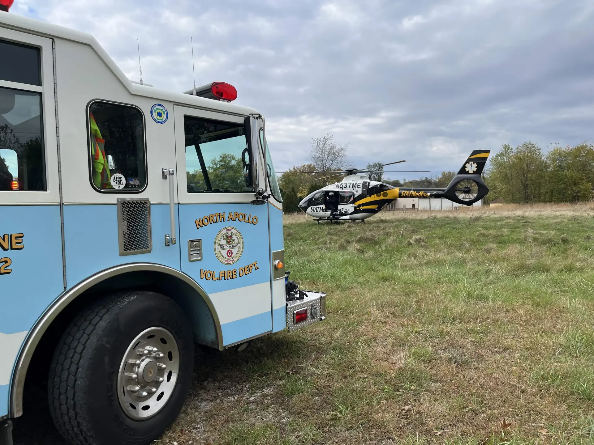 Department engine parked in a field beside a landed STAT MedEvac helicopter